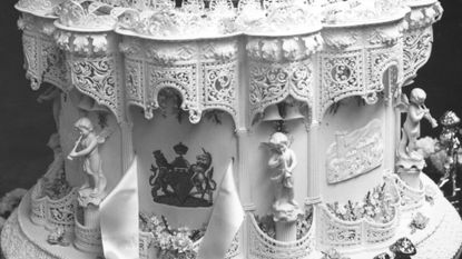 A black-and-white photo of a tiered wedding cake with cupids on it