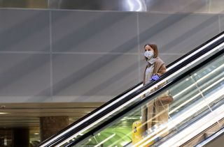 Woman travelling down the escalator at the airport wearing a face mask