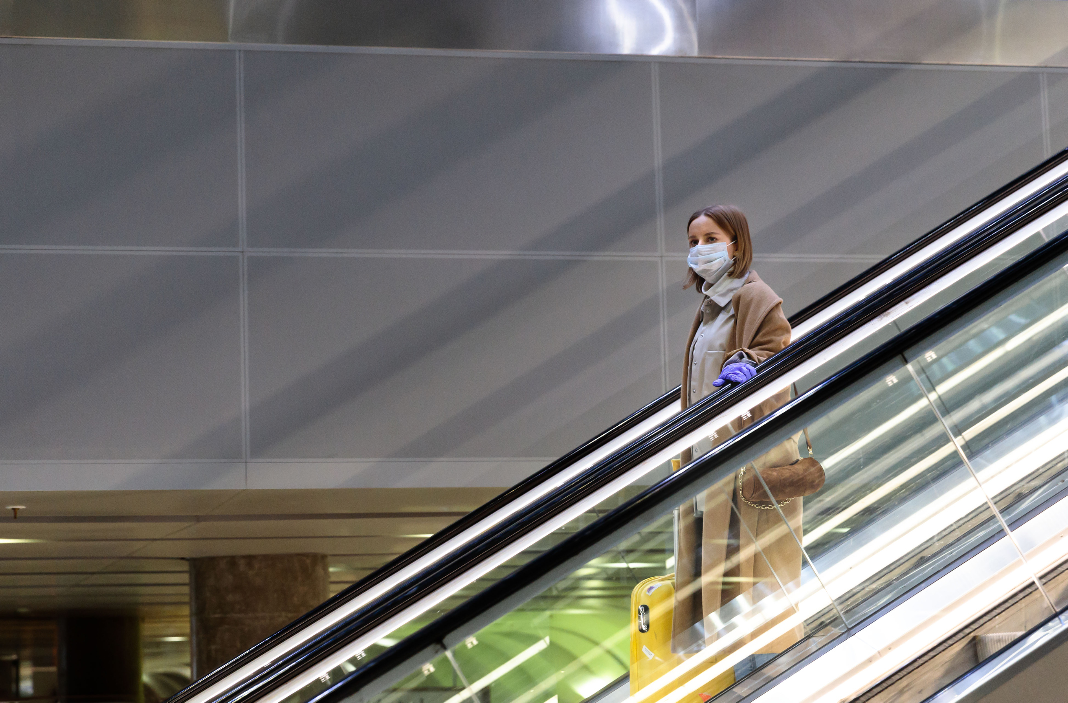 Woman travelling down the escalator at the airport wearing a face mask