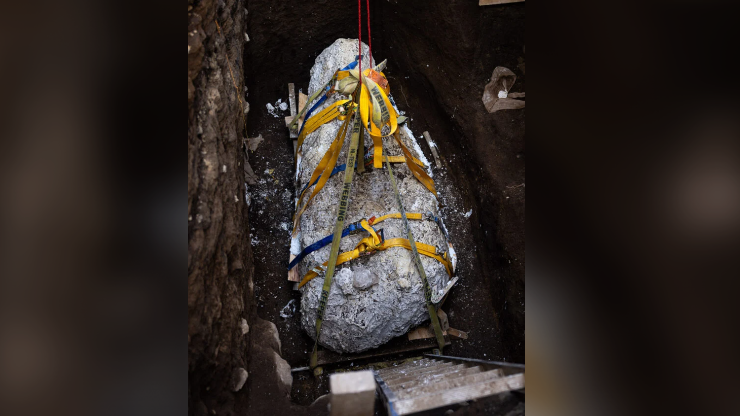 a bundle of white plaster is being hauled out of a deep ditch by means of yellow straps