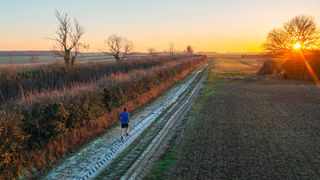 Elevated/drone view of a runner on a frosty trail from the UK countryside at sunset - 5 tips for night running