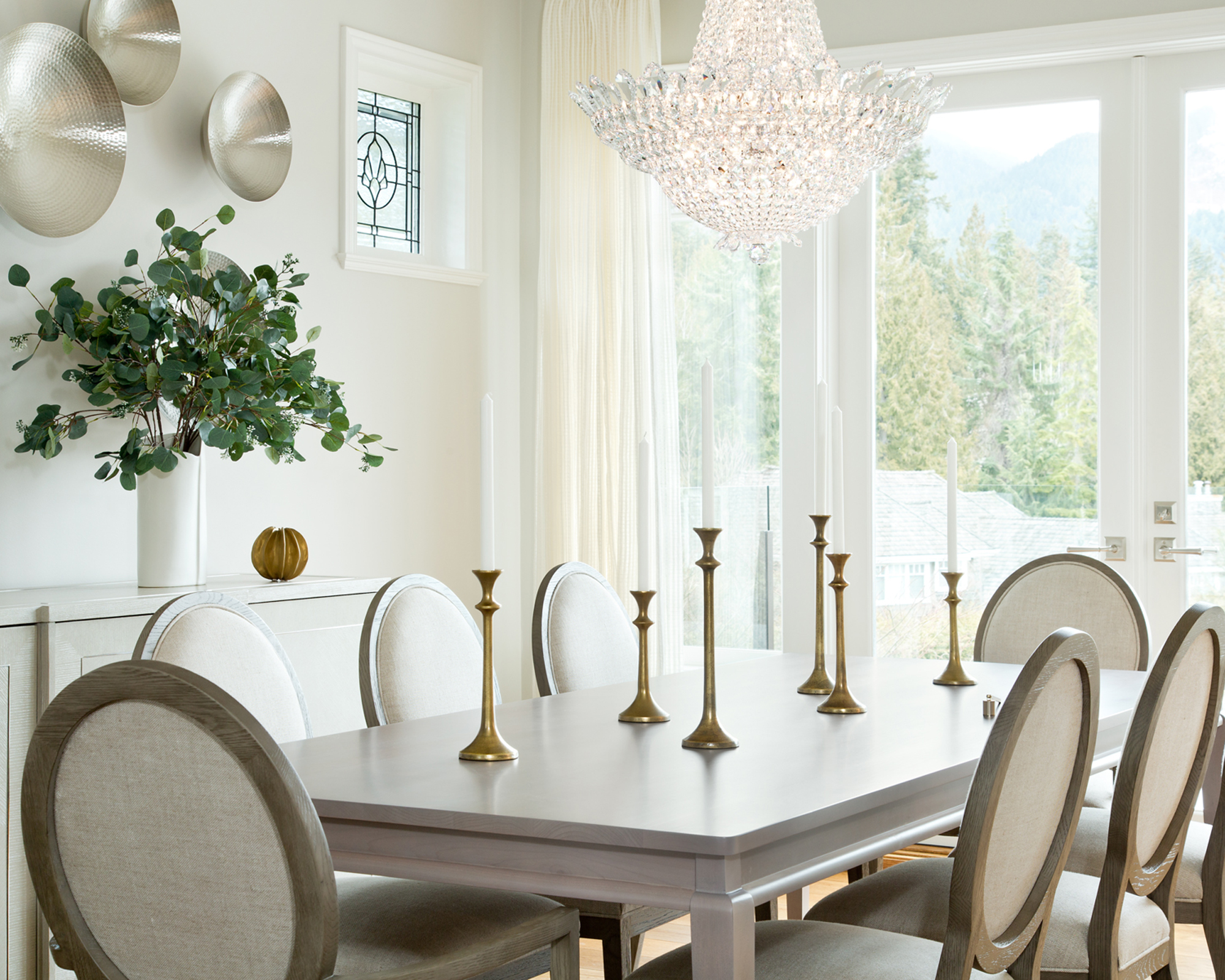 A small dining room idea with french windows, white curtains and walls and crystal chandelier over the table