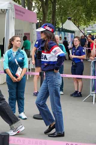 Kendall Jenner at the Paris Olympics wearing a USA hat, USA jacket, straight-leg jeans, black sunglasses, and black loafers.