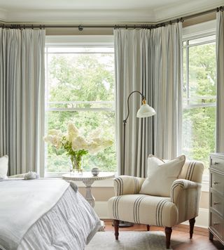 new england bedroom with linen covered chair with blue stripe