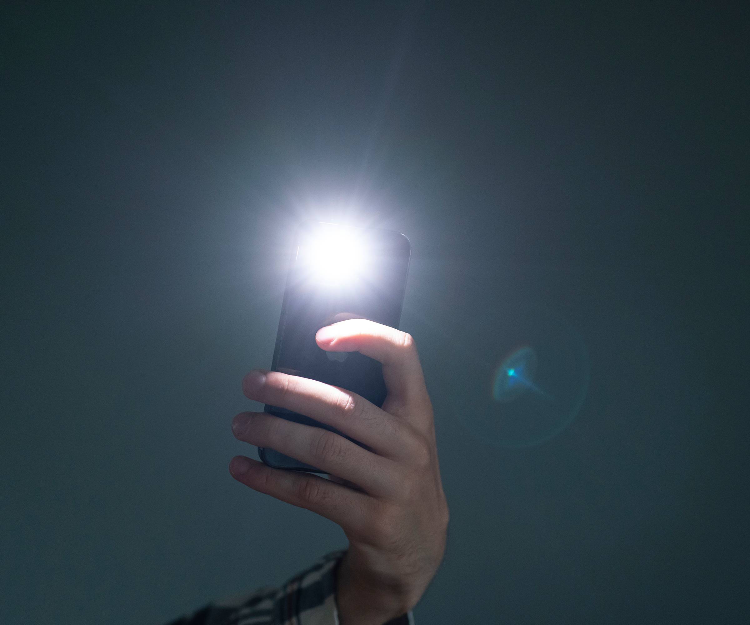 A hand holds a phone with the flashlight on