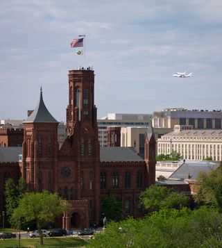 Space shuttle Discovery, mounted atop a NASA 747 Shuttle Carrier Aircraft (SCA) flies near the Smithsonian Institution Castle, Tuesday, April 17, 2012, in Washington.