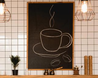 chalkboard with coffee mug on a white subway tile background above a wooden floating shelf