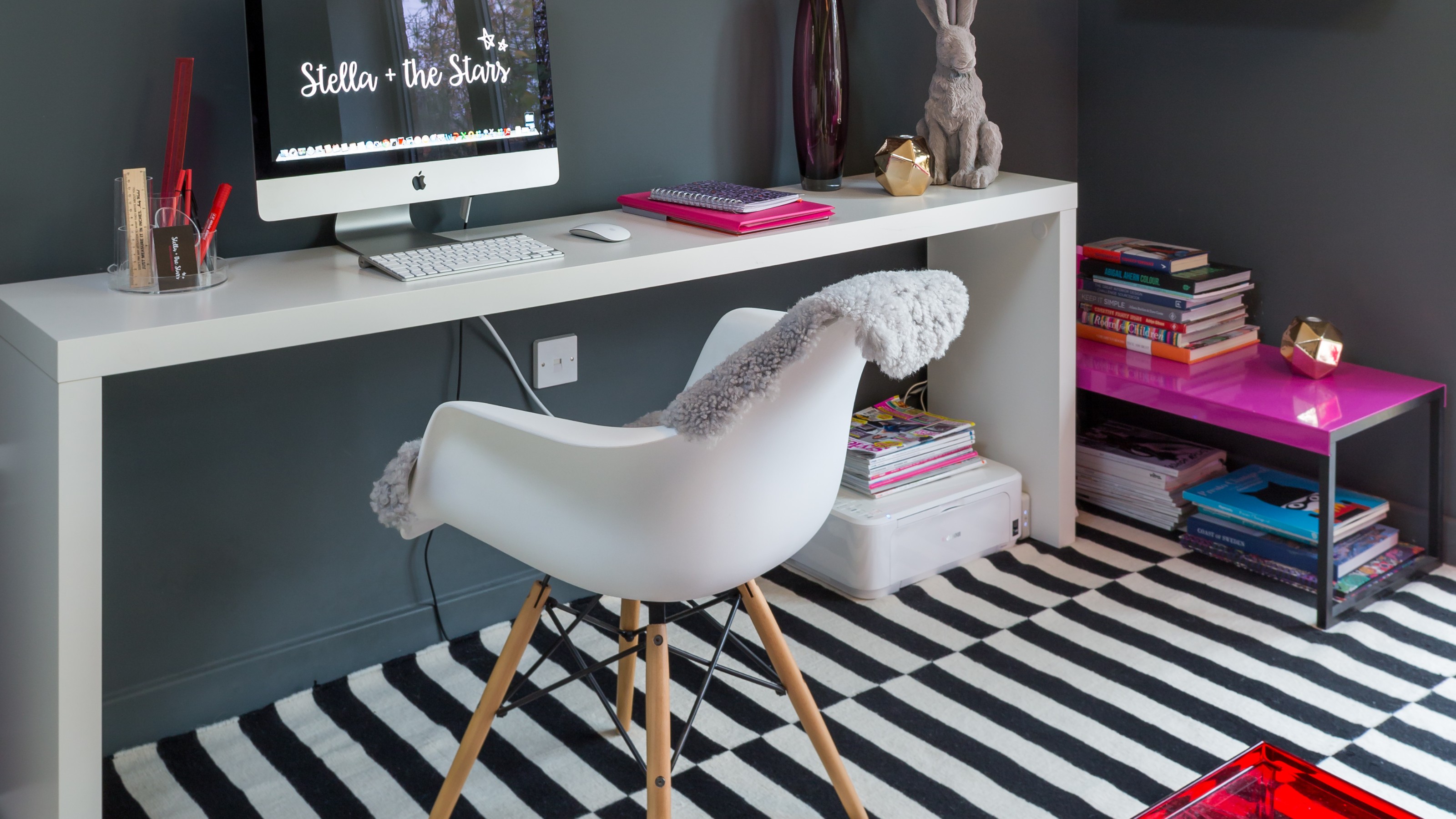 A grey-painted home office with a striped black and white rug, a white slim desk and a white chair