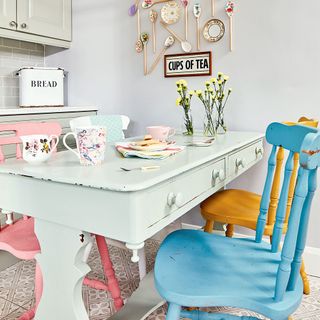 Pastel green painted kitchen table surrounded by colourfully painted chairs