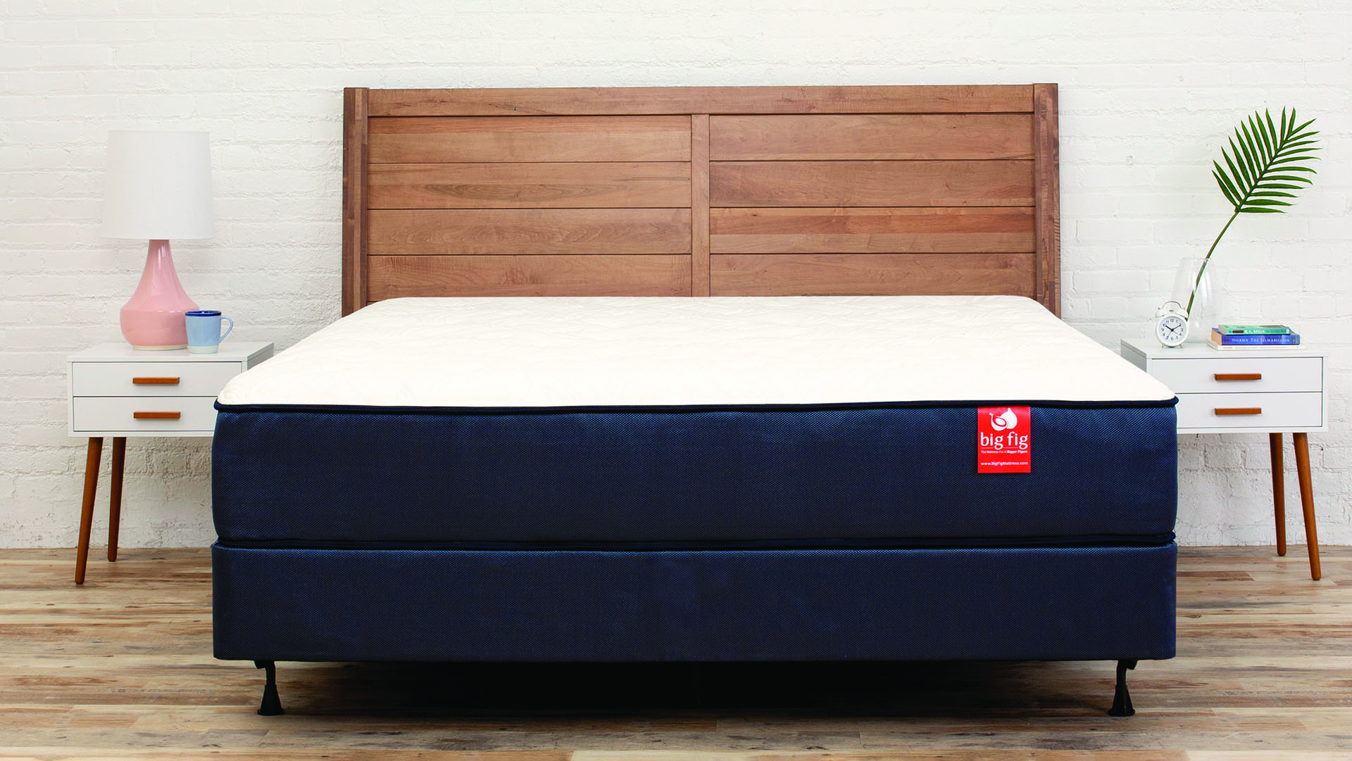 The Big Fig mattress for heavy people shown on a wooden bedframe next to white bedside cabinets