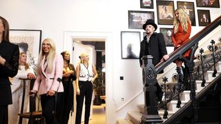 Boy George with guests in his living room as he stands on his black gothic styled staircase