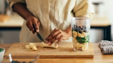 Woman's hands making protein shake with banana, blueberries, and spinach on a chopping board after learning how to lose weight without exercise