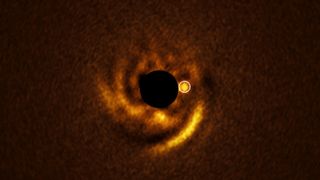 A golden ring of light surrounds a dark circle in the middle of the image with a golden smaller circle to the right