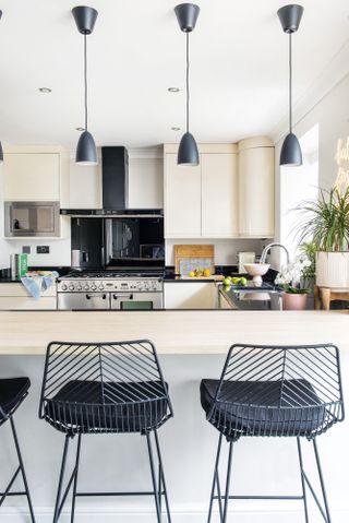 Cream kitchen with breakfast bar, black metal bar stools and four black pendant lights