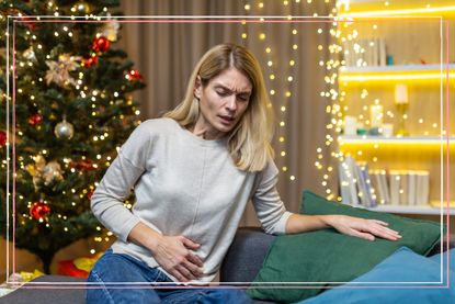A woman clutching her stomach in pain in front of a Christmas tree 