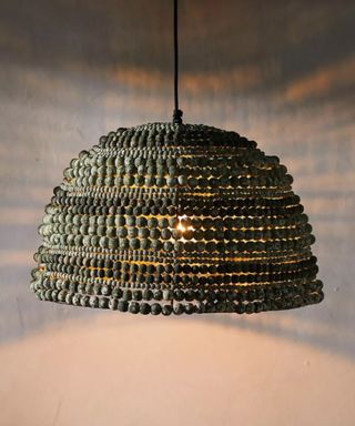 A moss green beaded pendant light in a semi-circle shape emitting a warm glow of light downwards