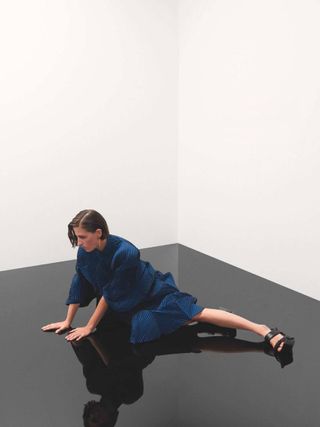 Image of woman in blue Issey Miyake pleats dress on black shiny floor