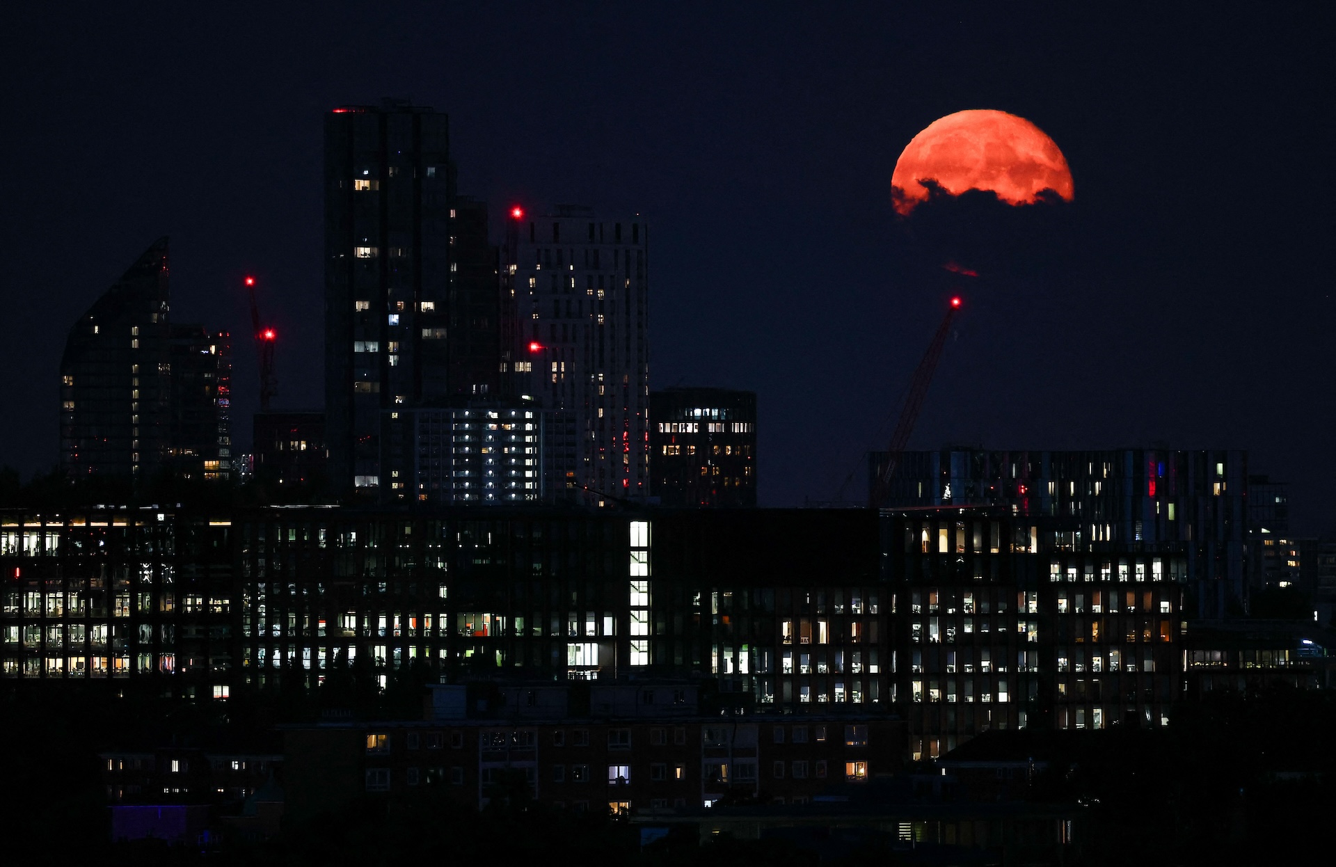 A red moon partially obscured by clouds hangs over the city lights of London