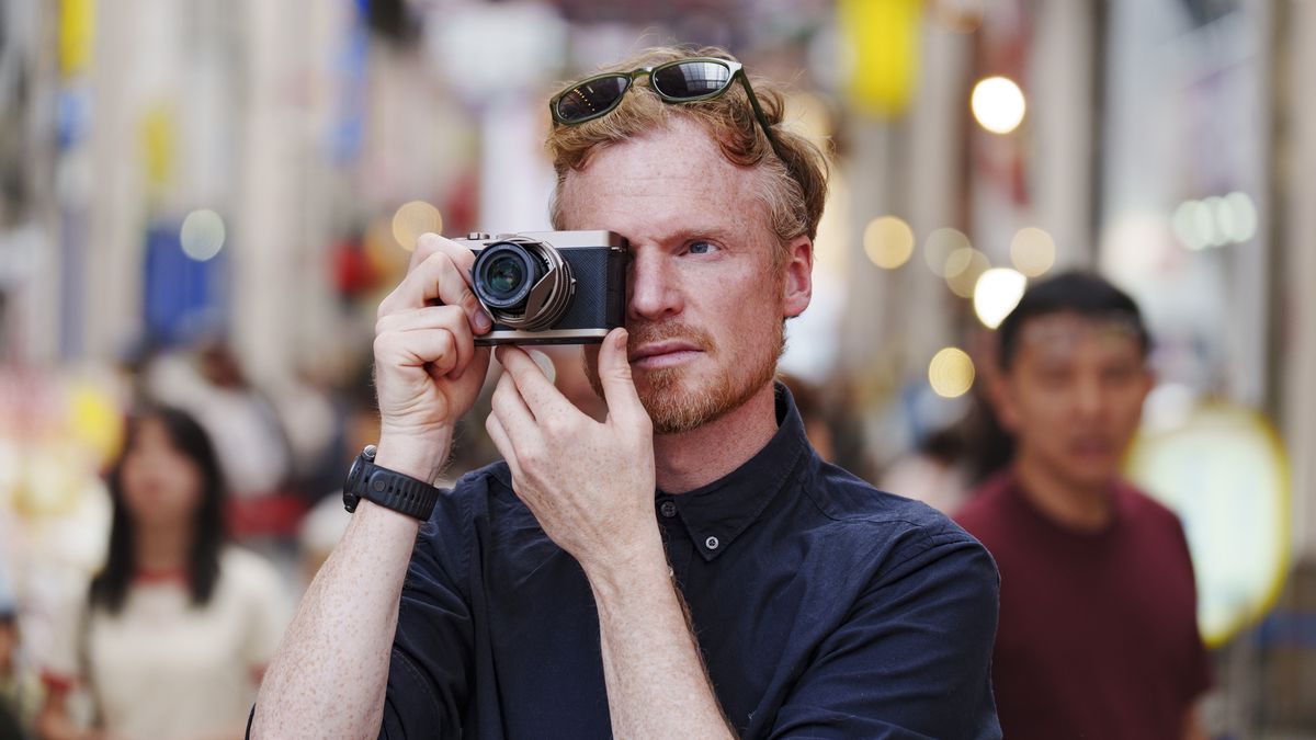 Man holding the Panasonic Lumix L10 compact camera up to his eye, he's looking through the viewfinder, in an urban setting of Japan