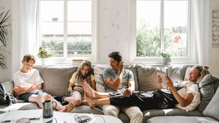 Family sitting on sofa at home using connected devices