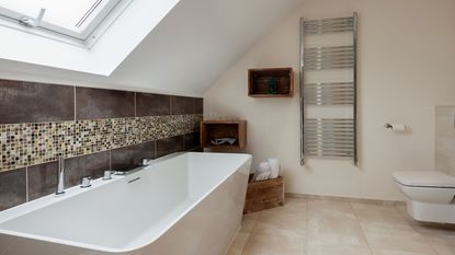 Chrome towel radiator in modern loft bathroom with dark tiling. around bath tub
