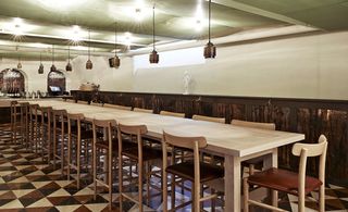 The Flying Elk, Stockholm, Sweden. A restaurant with a long table with high chairs next to it, pendant lights above it and triangular patterned floor tiles.