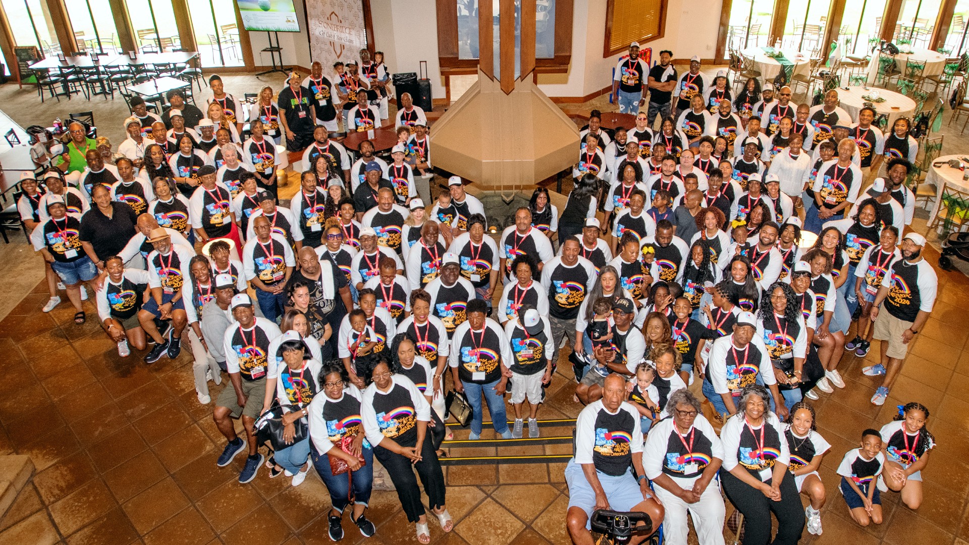 Picture from above of the Neal family reunion in 2024, New Orleans, Louisiana. About 100 people are posed, mostly in matching shirts and lanyards, looking up at the camera.