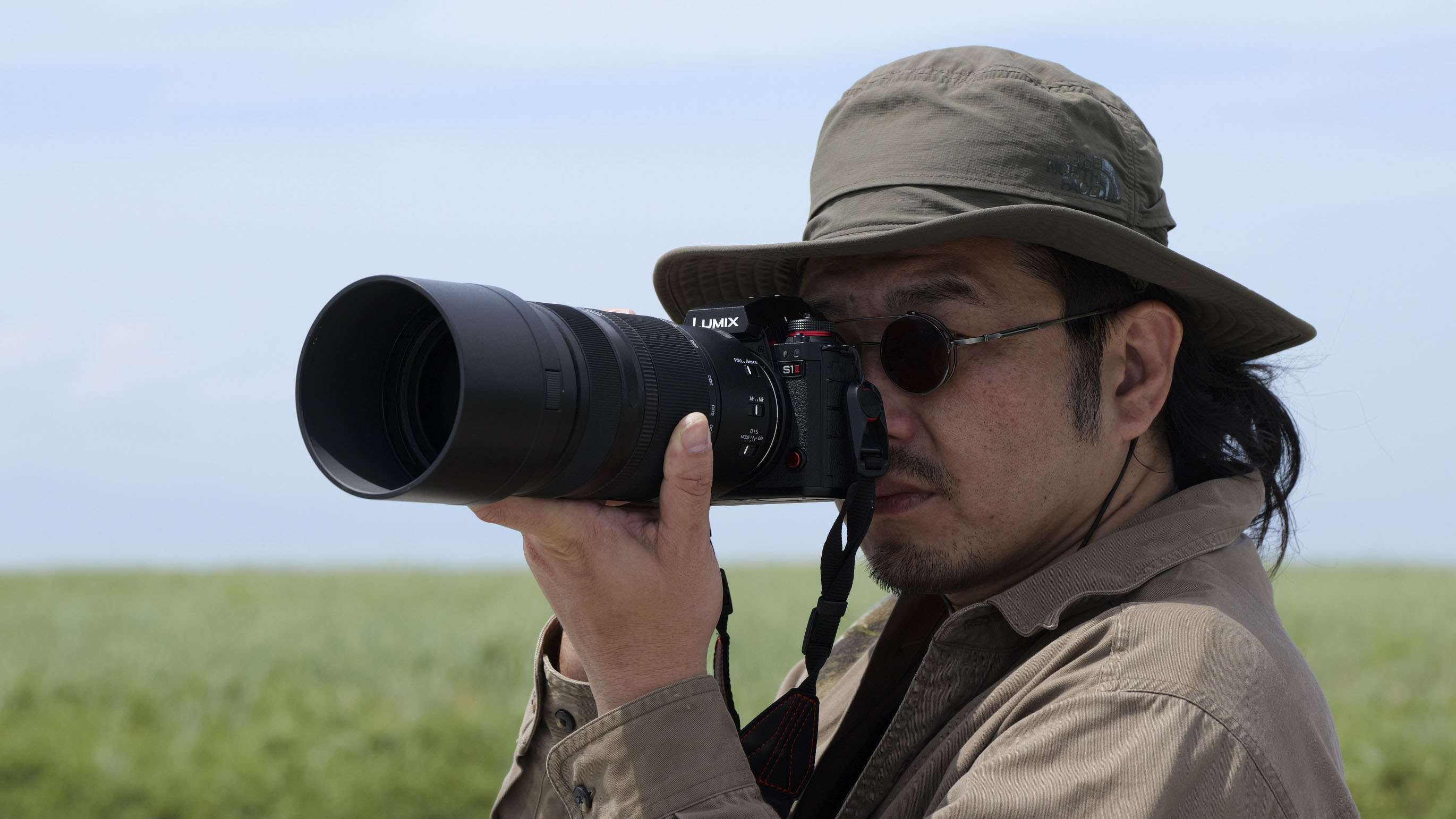 Panasonic Lumix S 100-500mm F5-7.1 O.I.S lens attached to a Lumix S1 II with photographer bringing the camera up to their eye
