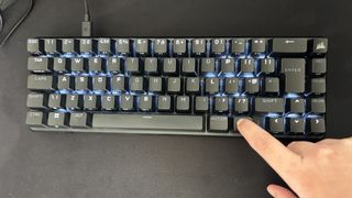 Finger holding Fn button on Corsair K65 Pro Mini RGB keyboard to show RGB lighting around dedicated keys