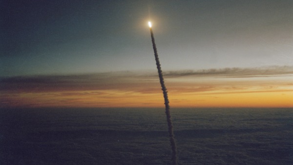 a rocket launch seen from afar as the sun is rising in the background