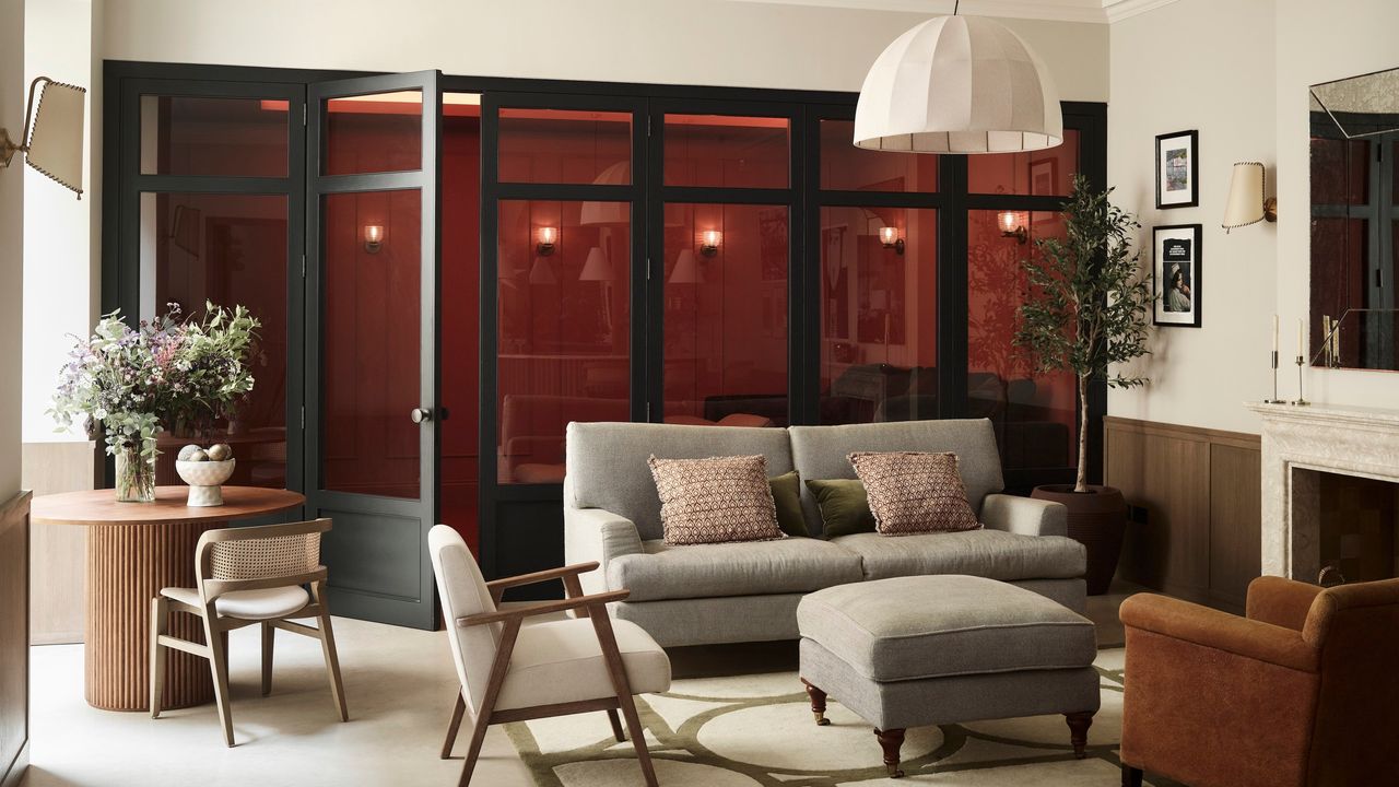 living room with a row of glass doors, pale walls, grey sofa and occasional chairs