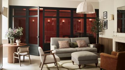 living room with a row of glass doors, pale walls, grey sofa and occasional chairs