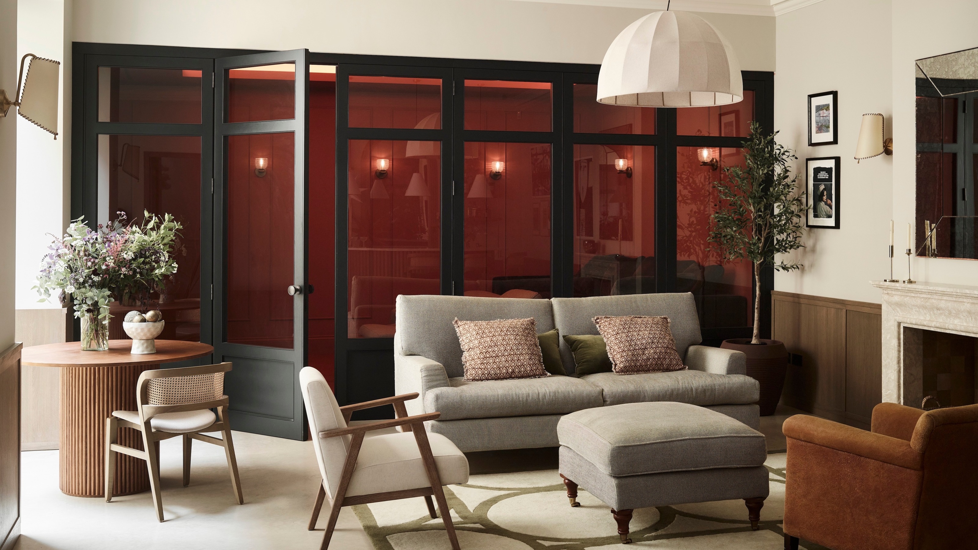 living room with a row of glass doors, pale walls, grey sofa and occasional chairs