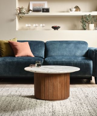 A living room with a dark blue couch, a marble coffee table with a wooden base, and a gray rug