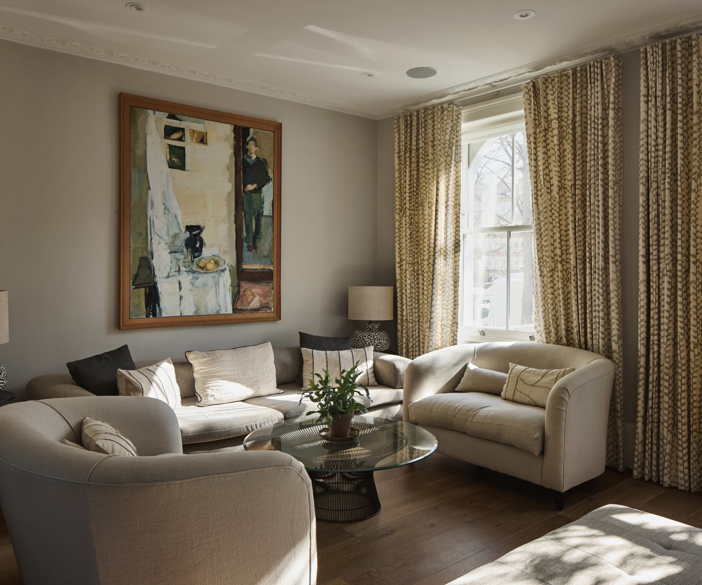 A living room with large curtains and three white sofas and a picture on the wall
