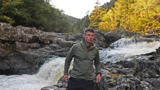 Hiker next to stream wearing a Montane Khamsin Hooded Softshell Jacket