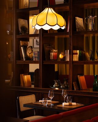 An Art Deco design-inspired Roman restaurant features flower-shaped pendant lights in orange, mid-century modern Eames furniture, and a selection of collectibles on its wooden shelves.