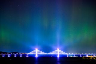 A green illuminated sky over a silver bridge