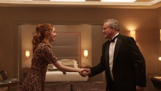 Karen Gillan in a brown floral dress as Madeline shakes hands with Hugh Bonneville in a dinner jacket as Douglas in Douglas is Cancelle