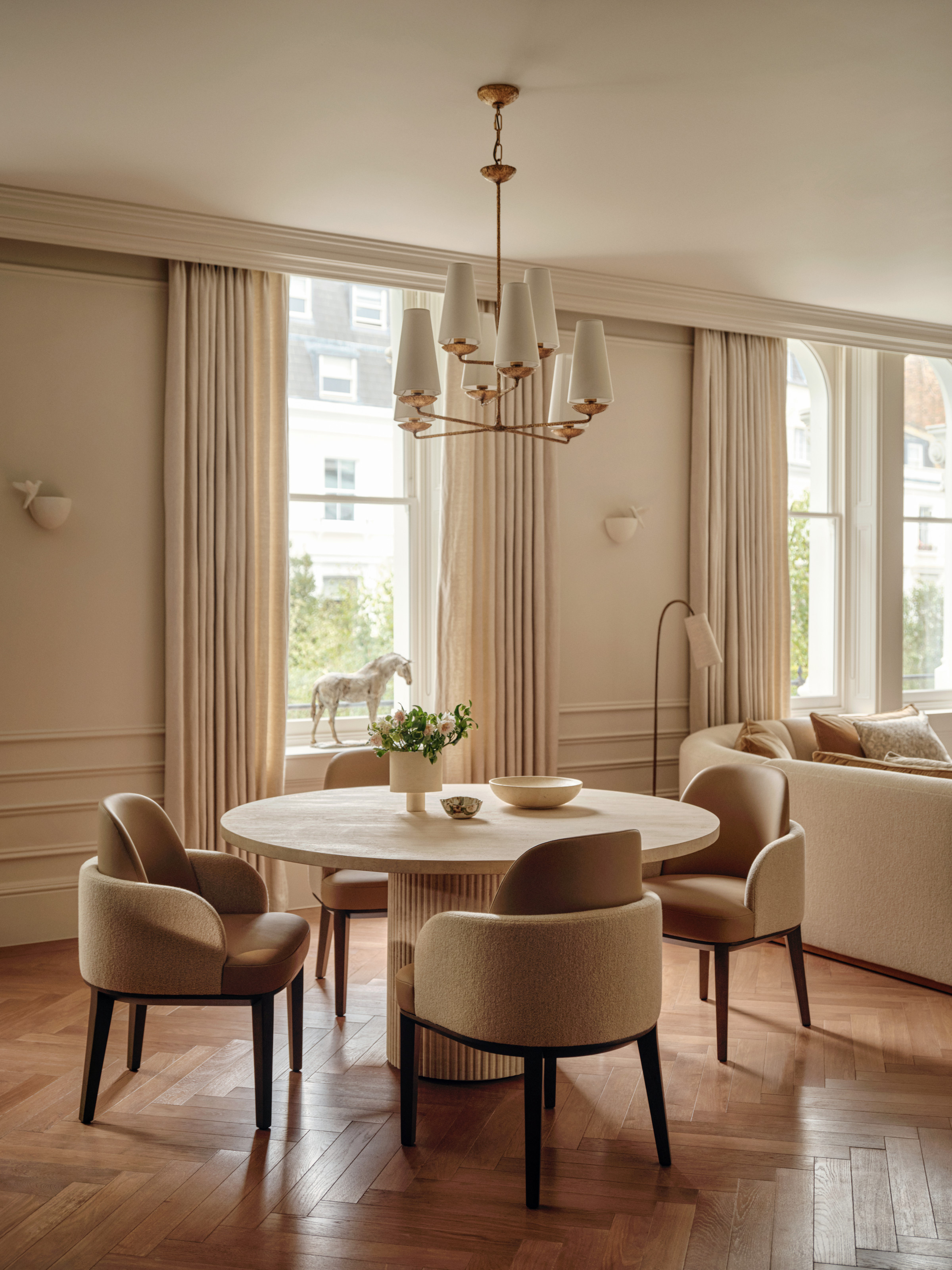Warm white dining room with travertine roudn table, curved chairs and chandelier
