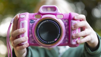 A pink V-Tech KidiZoom Duo camera in the hands of a young child