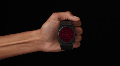 Hand holding a black watch with a red face against a black background