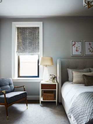 Light grey painted bedroom with grey upholstered bed and grey patterned Roman blinds