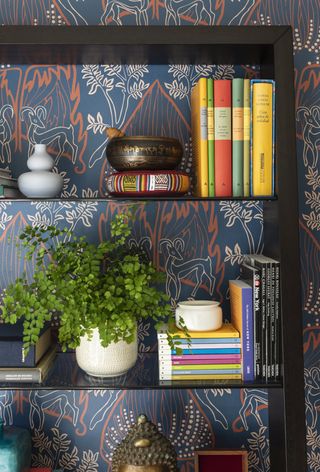 Black and glass bookshelves in front of nature pattern wallpaper in blue and coral
