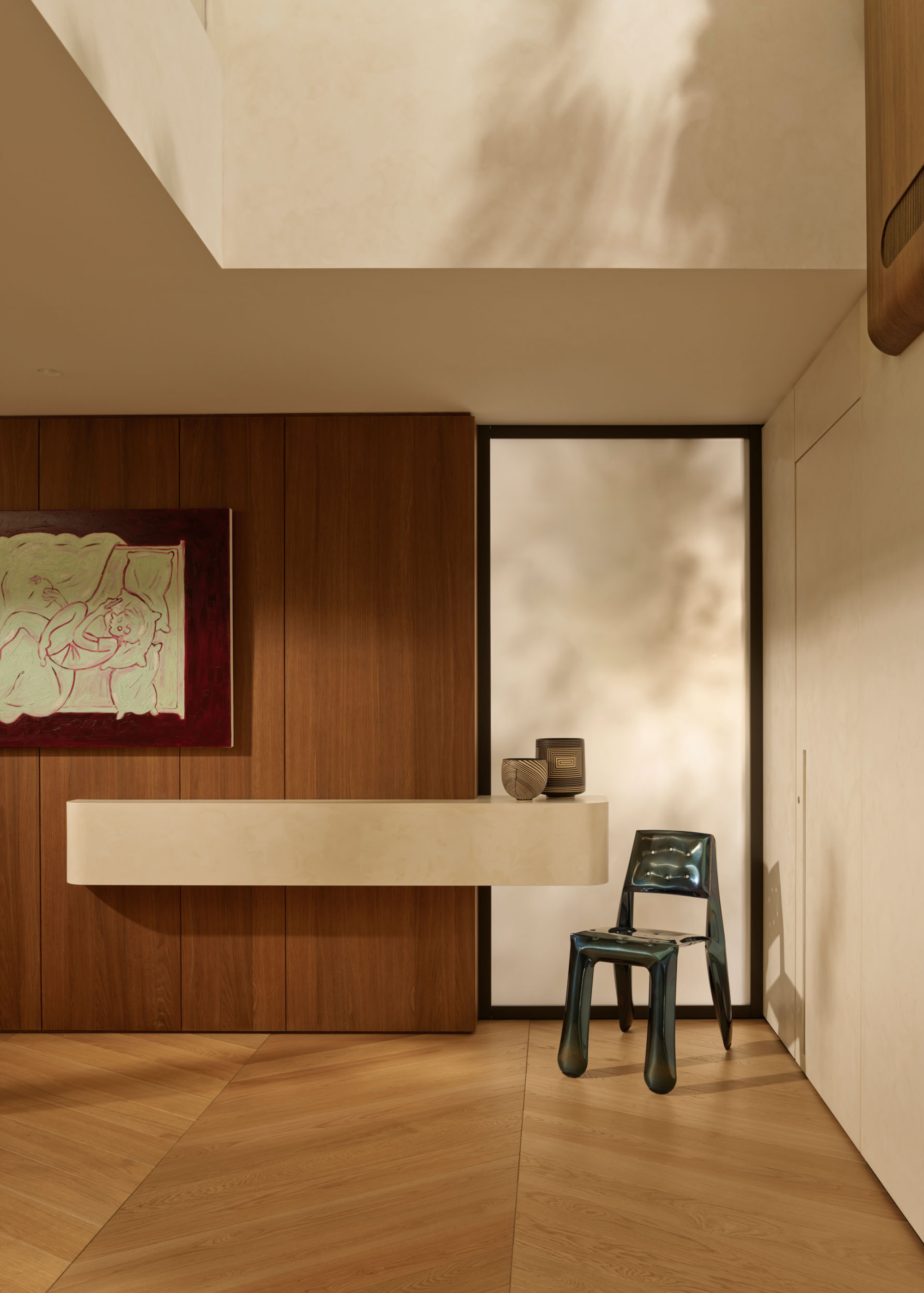 A living room corner by a floating white ledge with a pair of ceramic bowls by a metallic blue chair and below a red painting