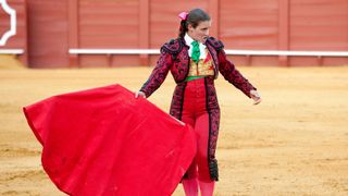 A female Matador in traditional clothing holding a red cape