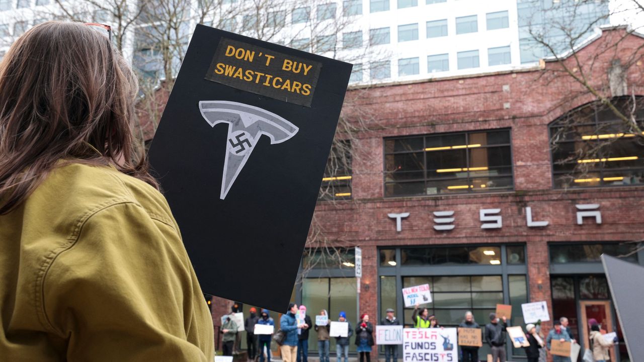 A woman holds a sign saying &quot;don&#039;t buy swastikas&quot; at a protest outside a Tesla showroom in Seattle