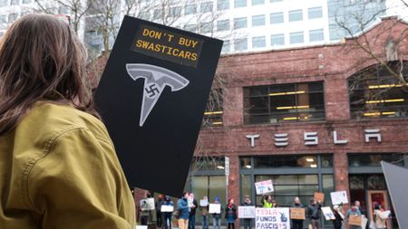 A woman holds a sign saying "don't buy swastikas" at a protest outside a Tesla showroom in Seattle