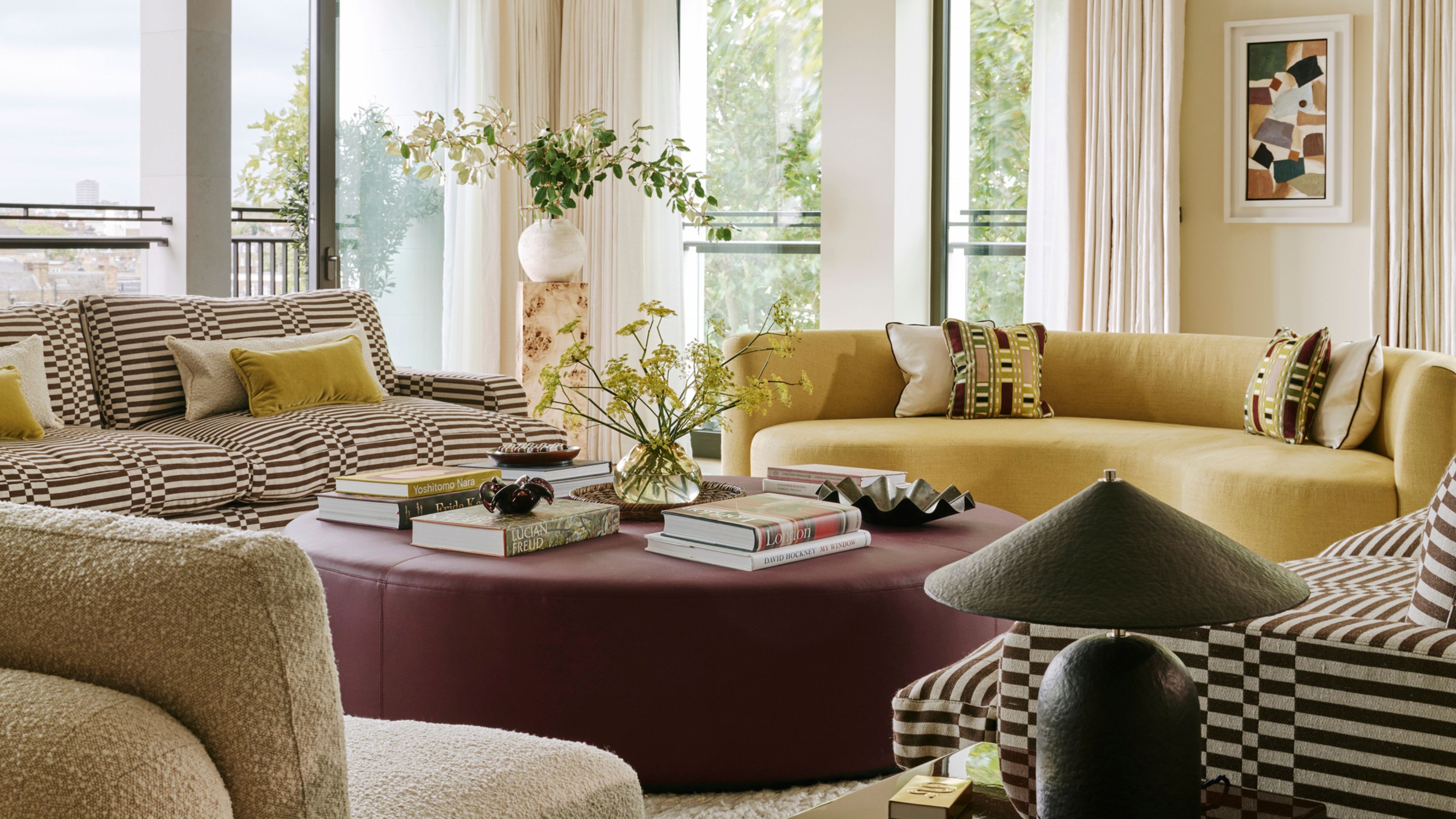 a colorful living room with more muted colors of yellows, browns, reds and creams in a modern aesthetic with round pouf table and a curved sofa and seating around it