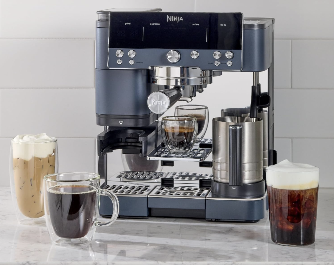 A Ninja espresso and coffee machine sitting on a white marble countertop surrounded by four different prepared beverages, including hot black coffee, iced coffee with foam, and iced latte.